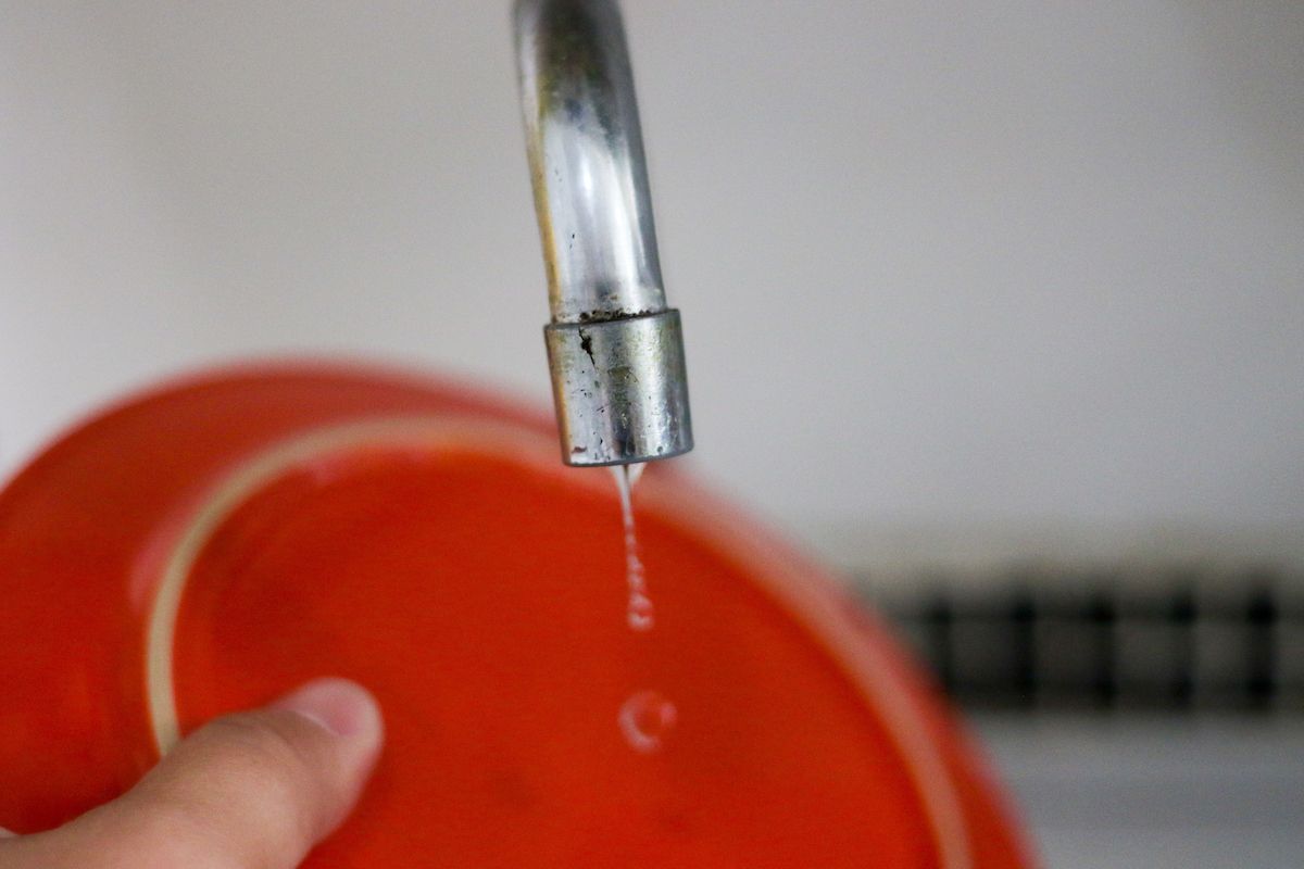 A foto mostra um prato laranja sendo lavado debixo de uma torneira