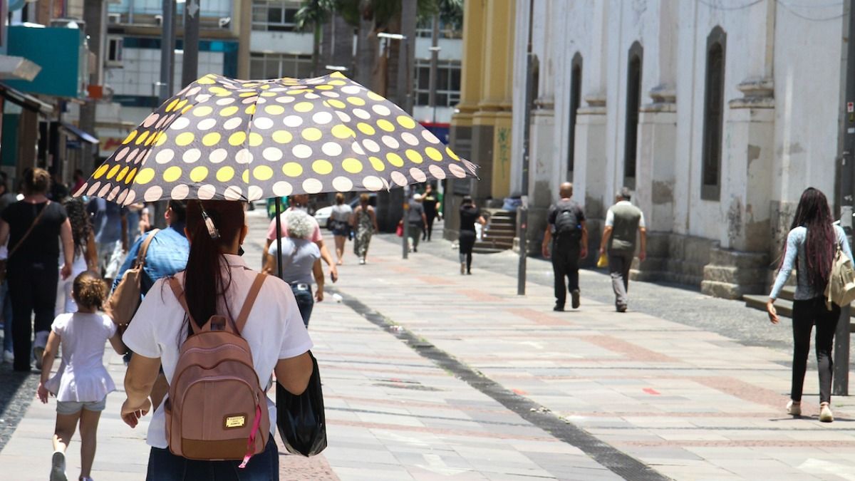 uma mulher caminha com uma sombrinha para se proteger do sol forte