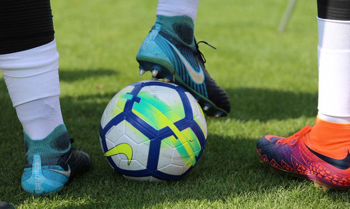 A foto mostra pernas de jogadores de futebol segurando uma bola