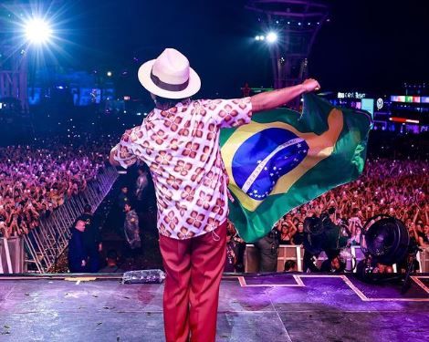 a foto mostra o cantor segurando uma bandeira do Brasil no palco