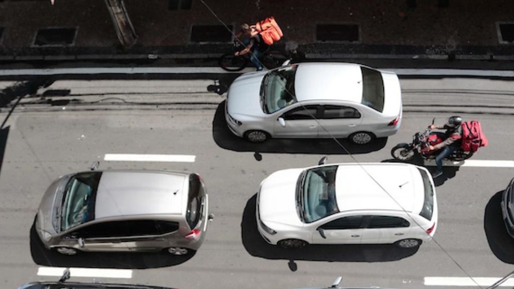 a foto mostra o teto de três carros em uma avenida da cidade. Ao lado do veículos passa um entregador