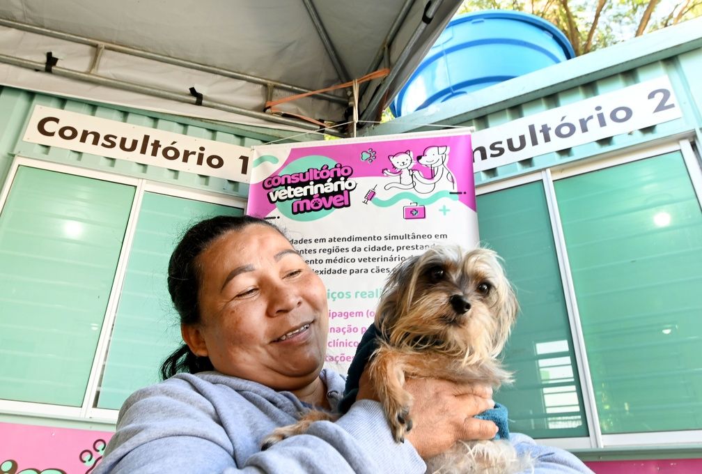 a foto mostra uma mulher segurando um cachorro no colo enquanto espera por atendimento