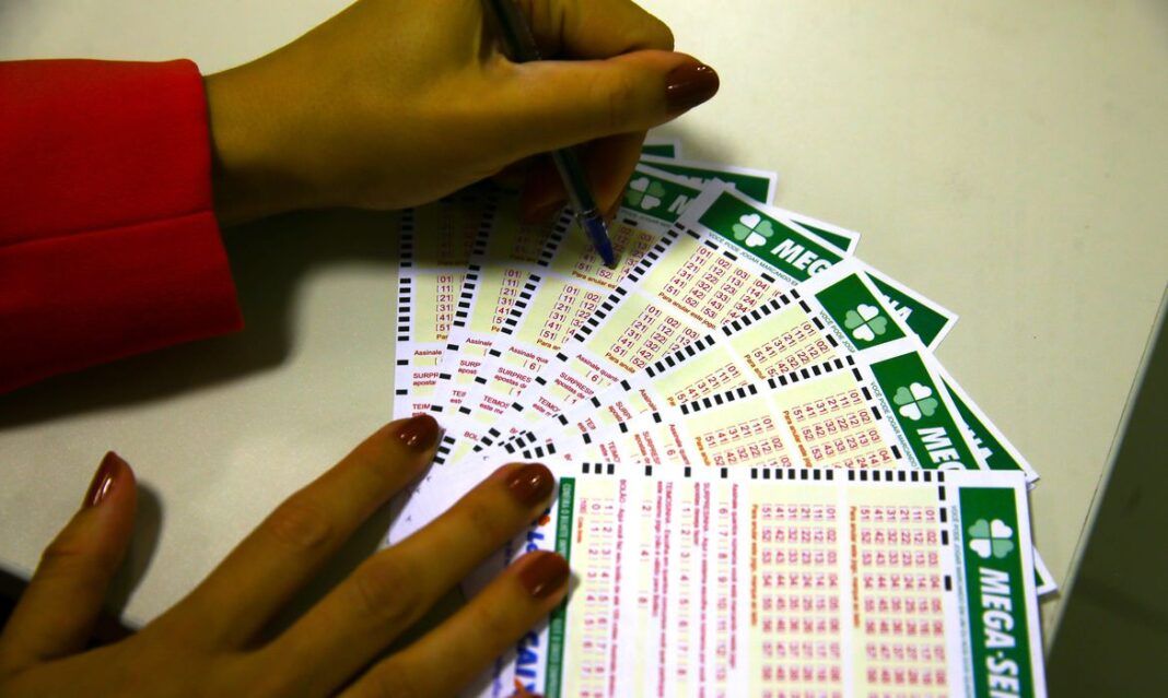a foto mostra a mão de uma pessoa marcando com uma caneta cartões de aposta da Mega-Sena