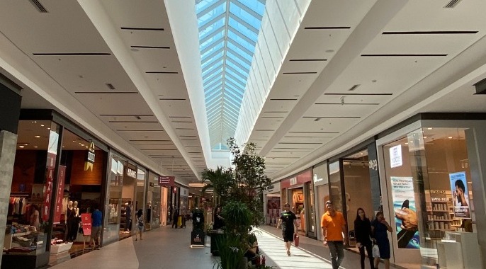 A foto mostra o corredor de um shopping com pessoas camiinhando