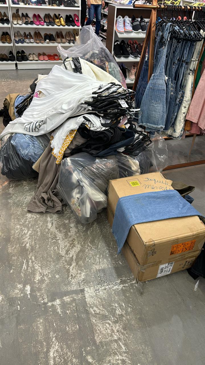 A foto mostra diversas roupas, cabides e caixas que foram apreendidos pela Polícia