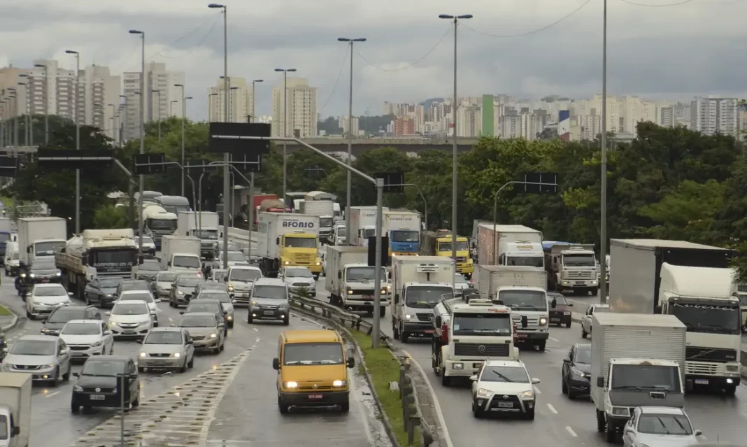 A foto mostra diversos veículos, entre carros, caminhões e utilitários, em uma avenida na capital paulista