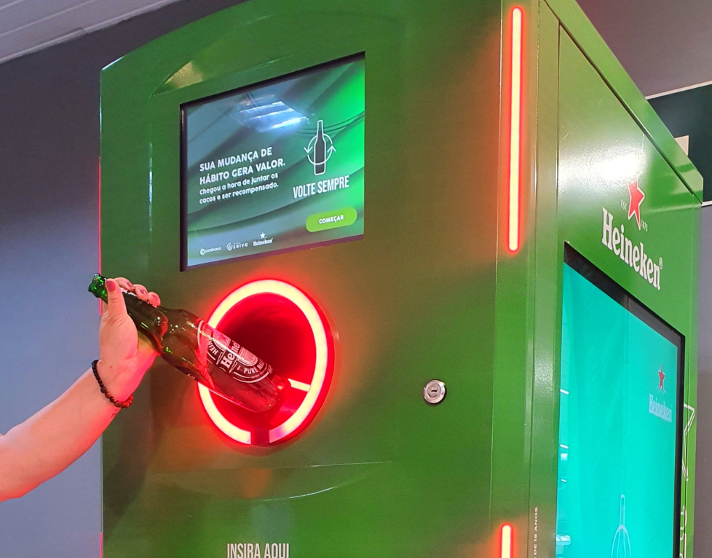 foto mostra o braço de uma pessoa depositando uma garrafa de cerveja da Heineken na máquina coletora