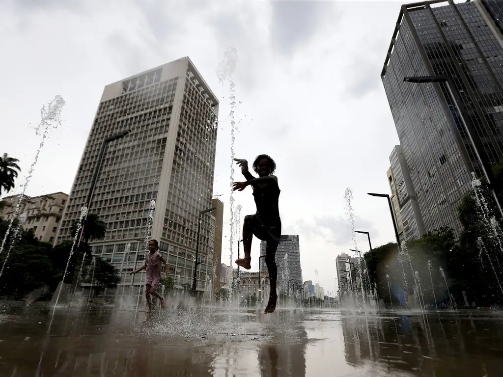A foto modstra uma criança pulando com prédios ao fundo