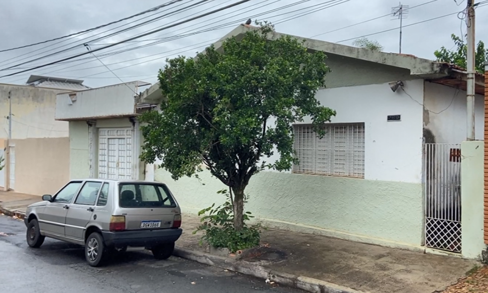a foto mostra a frente de uma casa em uma rua, onde há uma árvore e um carro estacionado