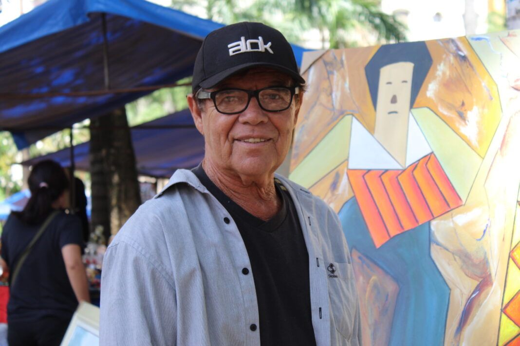 Artista Nelson Theodoro em frente a uma obra autoral na Feira Hippie