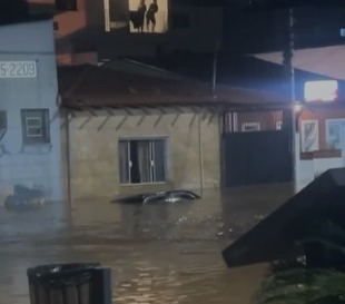 a imagem mostra rua compeltametne alagada com carro coberto de água até o teto