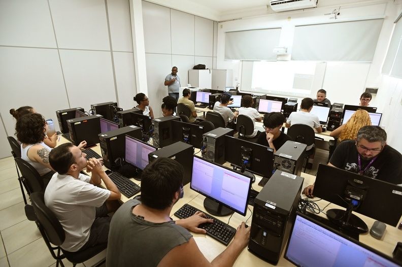 a foto mostra vários estudantes usando seus computadores em uma sala