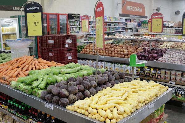 A foto mostra uma banca com frutas e legumes dentro de um supermercado