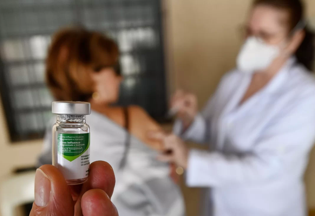 a foto mostra uma ampola com o imunizante e uma pessoa sendo vacinada atrás