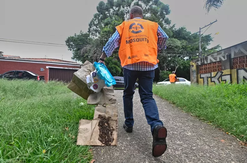 a foto mostra uma gente de saúde recolhendo objetos que podem se tornar criadouros da dengue