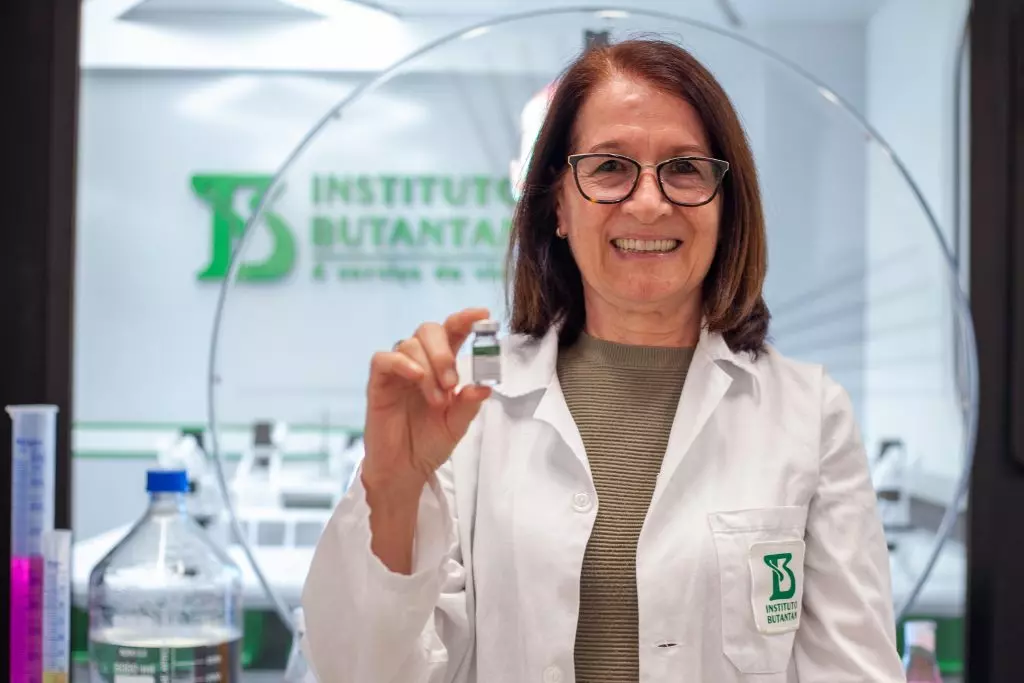 a foto mostra a pesquisadora que segura um frasco de vacina e sorri