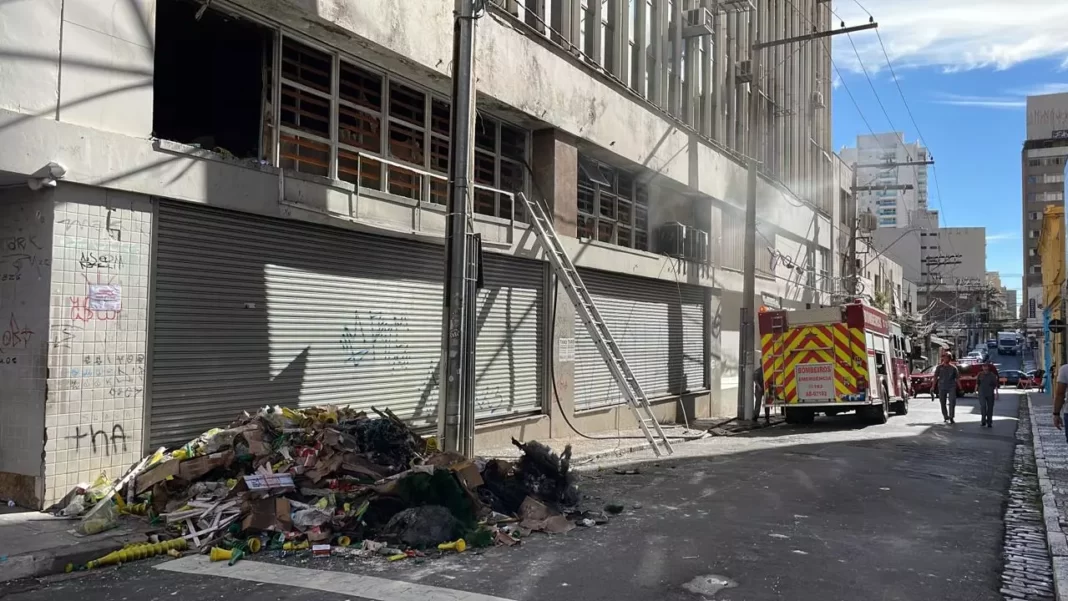 A foto mostra o prédio incendiado com uma viatura do Corpo de Bombeiros na frente