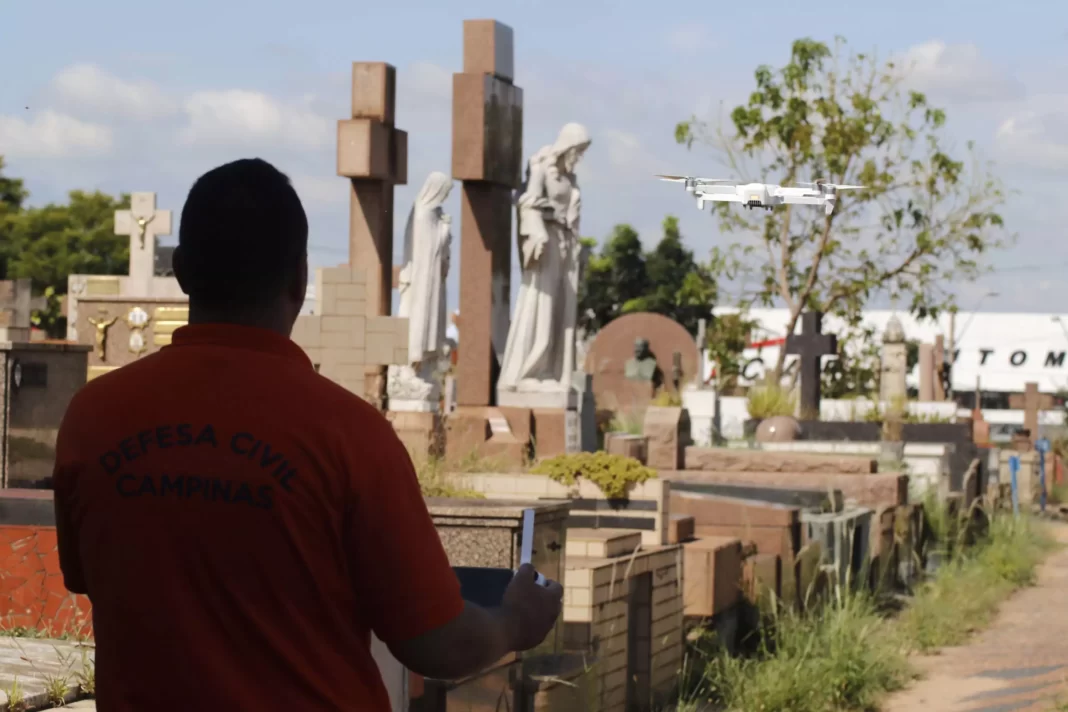 A imagem mostra um homem operando um drone no cemitério, em Campinas