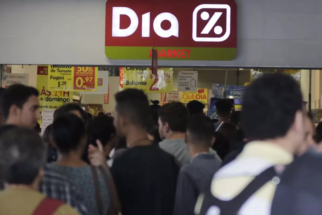 a foto mostra diversas pessoas em frente a uma unidade da rede de supermercados dia