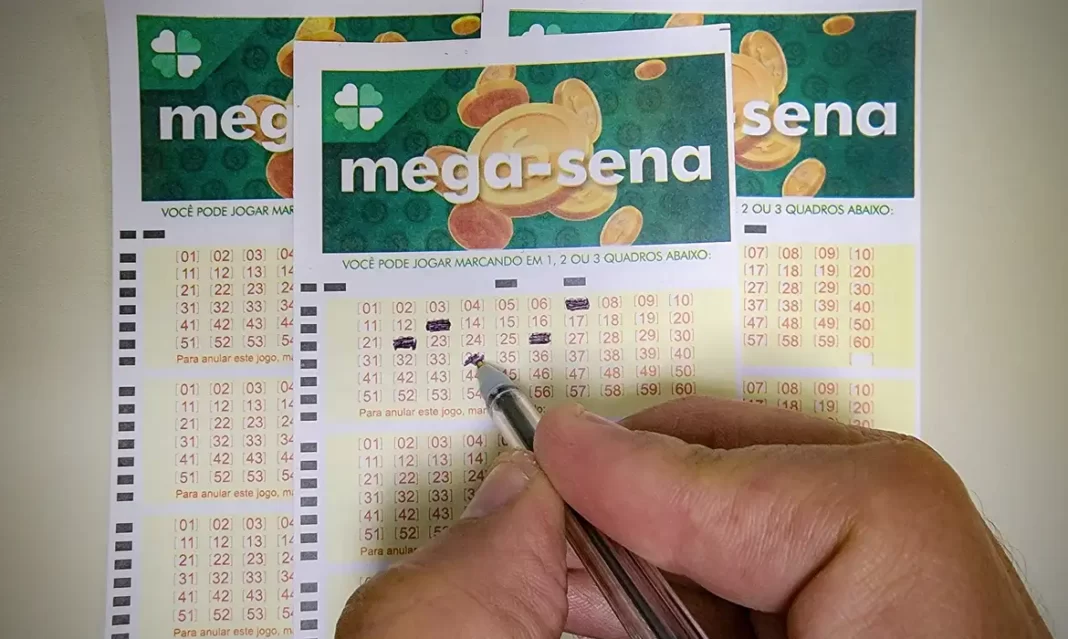 a foto mostra a mão de uma pessoa segurando uma caneta, marcando um cartão de apostas da Mega-Sena