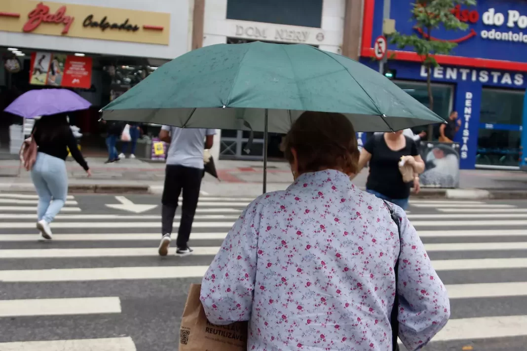 a foto mostra uma pessoa atravessando a rua com um guarda-chuva - alerta temporais