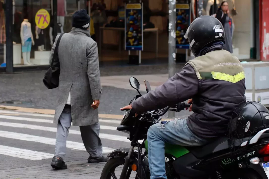 a foto mostra um motoqueiro parado no semáforo, enquanto um pedestre atravessa a rua - frente fria