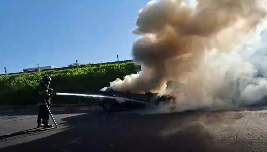 a foto mostra um bombeiros tentando apagar o fogo do carro e muita fumaça saindo do local