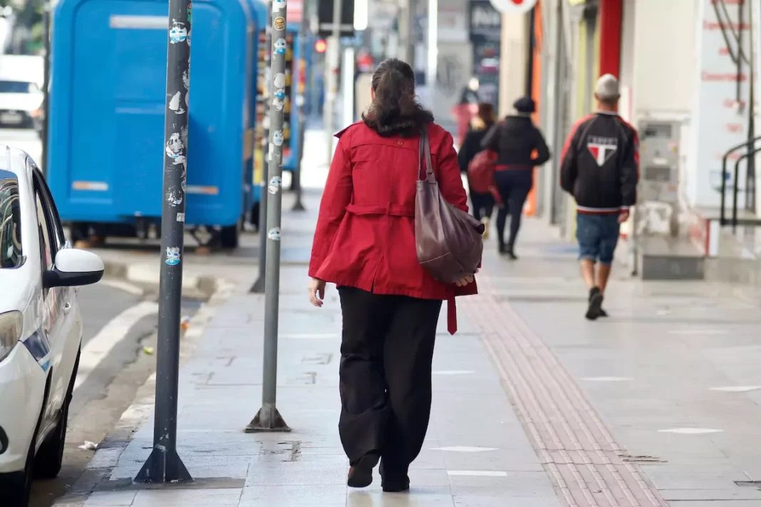 a foto mostra uma mulher com agasalho caminhando em uma calçada