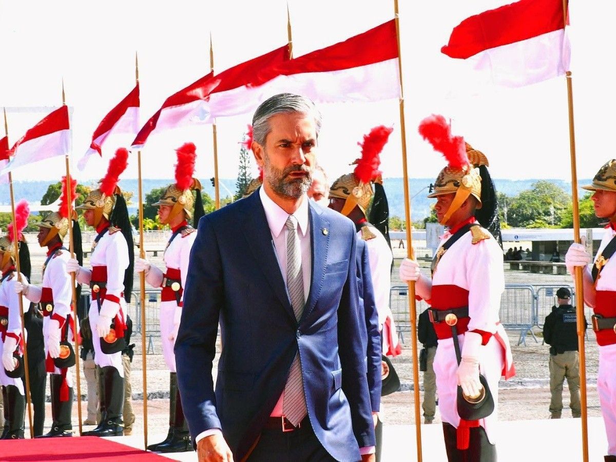 No centro da imagem, Augusto de Arruda Botelho aparece na rampa do Palácio do Planalto. Ao fundo, soldados da guarda presidencial Dragões da Independência aparecem com fardamento branco e vermelho.