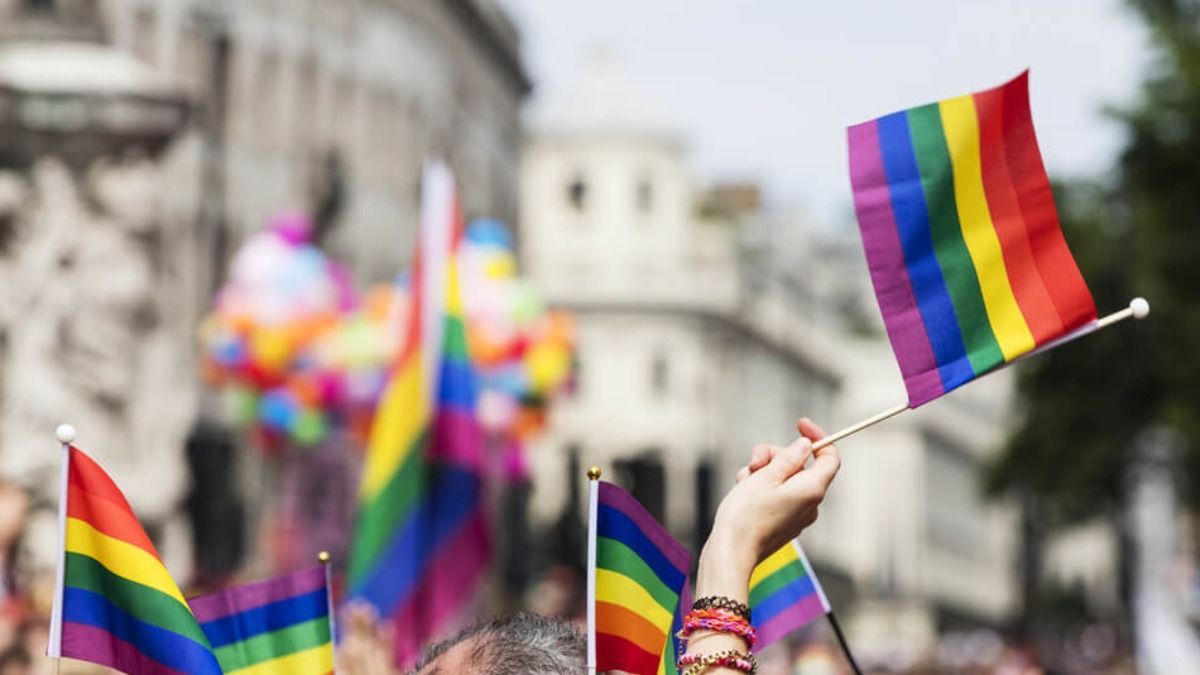Mãos seguram bandeiras da cor do arco-íris, relacionada ao movimento LGBTQIAP+.