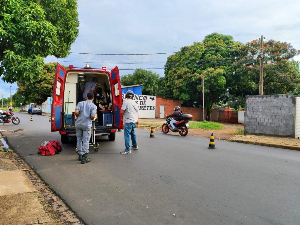 A foto mostra uma moto vermelha e uma ambulância vermelha dos Bombeiros em via pública, com pessoas sendo socorridas