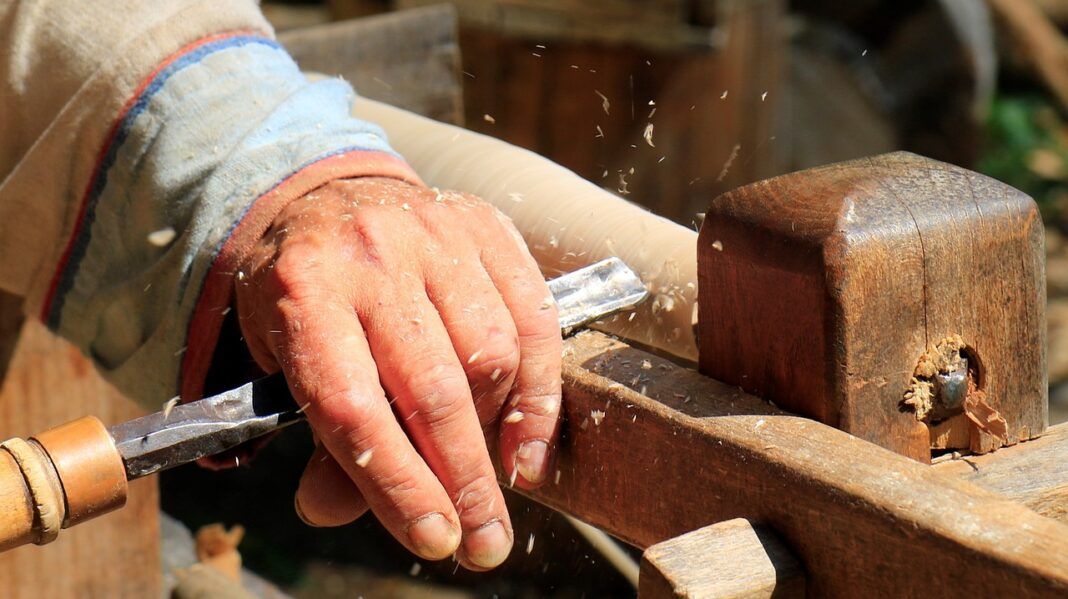 A foto mostra a mão de uma pessoa branca praticando serviços de carpintaria