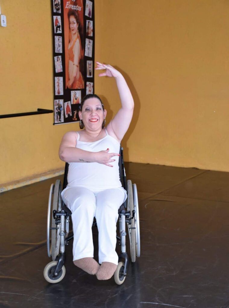 A foto mostra uma dançarina cadeirante com roupas brancas