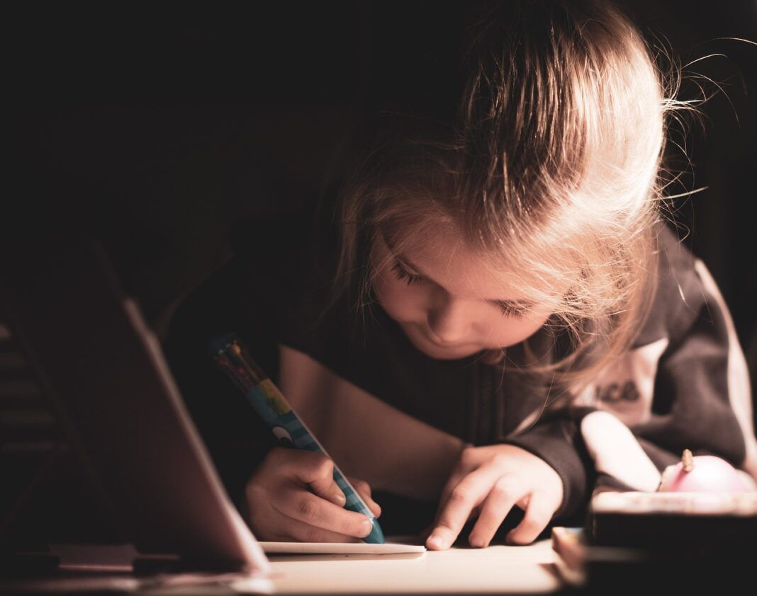 A foto mostra uma criança escrevendo em um papel