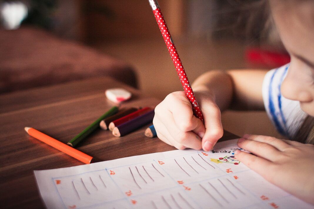 A foto mostra a mão de uma criança escrevendo em um papel
