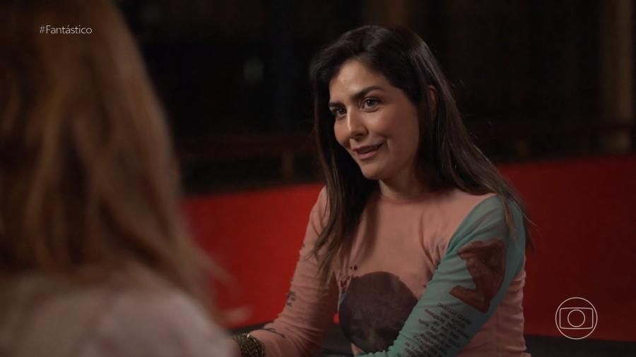 Leticia Sabatella está vestindo uma roupa de blusa de frio com uma manga verde e está conversando com uma repórter do Fantástico